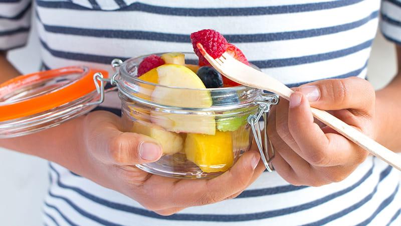 close up of hands eating fruit in a mason jar with fork